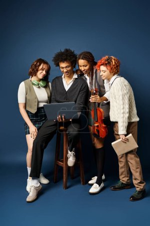 Foto de Amigos multiculturales se reúnen alrededor de la computadora portátil con un atuendo elegante, cautivado por la pantalla, sobre un fondo azul oscuro. - Imagen libre de derechos