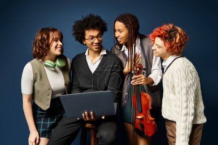 Young multicultural friends, standing together in stylish attire, collaborating around a laptop on a dark blue background.