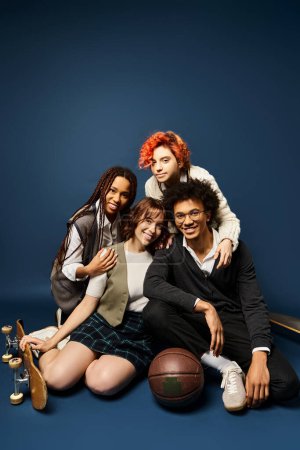 Foto de Grupo multicultural de jóvenes amigos, sentados juntos con un atuendo elegante sobre un fondo azul oscuro. - Imagen libre de derechos