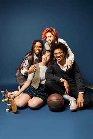 A group of stylishly dressed young multicultural friends, including a nonbinary person, sit closely together on a dark blue background.