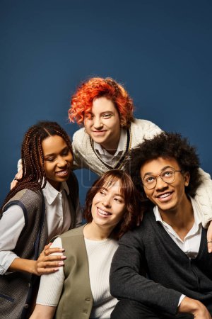 A group of young multicultural friends, including a nonbinary person, posing in stylish attire on a dark blue background.