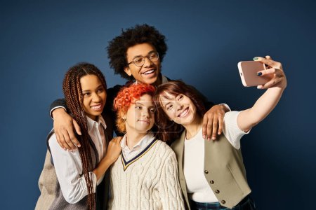 Multicultural friends, including a nonbinary individual, standing together, capturing a memory with a cell phone on a dark blue background.