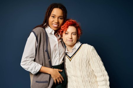 Foto de Dos jóvenes amigos multiculturales, incluyendo una persona no binaria, se mantienen unidos con un atuendo elegante sobre un fondo azul oscuro. - Imagen libre de derechos