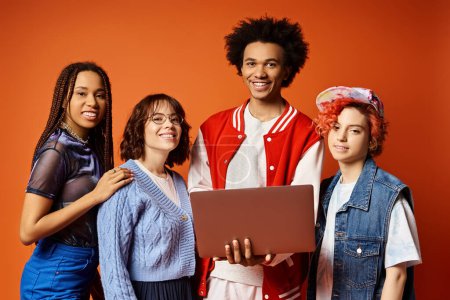 Photo for Young multicultural friends, including a nonbinary person, standing together in stylish attire with laptop in a studio setting, embodying unity and diversity. - Royalty Free Image