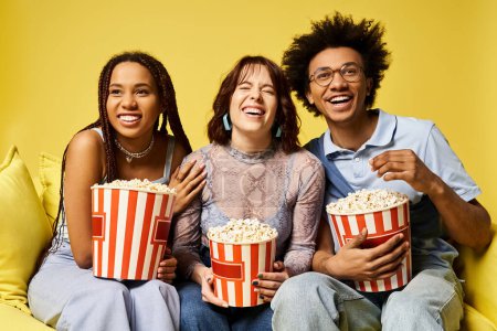 Multicultural young friends sitting on a couch, holding popcorn buckets, enjoying a movie night together.