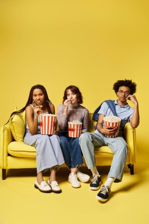 Foto de Tres jóvenes amigos multiculturales sentados en un sofá, comiendo palomitas de maíz y disfrutando de una noche de cine juntos en un ambiente acogedor. - Imagen libre de derechos