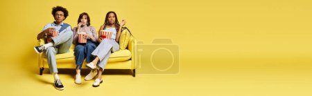 Eine Gruppe junger multikultureller Freunde, darunter eine nicht binäre Person, sitzt stilvoll auf einem leuchtend gelben Stuhl in einem Studio-Ambiente..