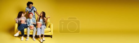 Photo for A group of young multicultural friends in stylish attire sitting together on top of a yellow chair in a studio setting. - Royalty Free Image