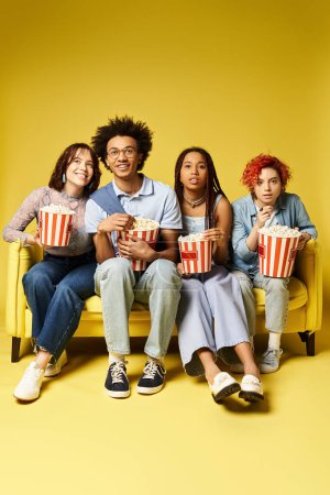 Foto de Jóvenes amigos multiculturales, incluyendo una persona no binaria, sentados juntos con estilo en un sofá de color amarillo brillante en un entorno de estudio. - Imagen libre de derechos