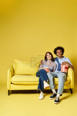 Foto de A man and a woman are seated on a vibrant yellow couch, chatting and enjoying each others company in a cozy setting. - Imagen libre de derechos