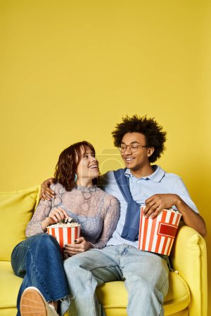 Foto de Un hombre y una mujer con un atuendo elegante relajándose en un sofá amarillo, disfrutando de un momento de paz y unión en un estudio luminoso. - Imagen libre de derechos