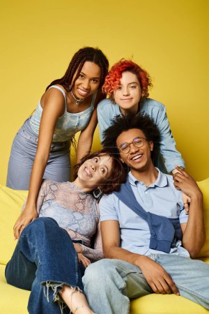 Téléchargez les photos : Un groupe diversifié de jeunes amis en tenue élégante assis sur un canapé jaune vif dans un cadre de studio. - en image libre de droit