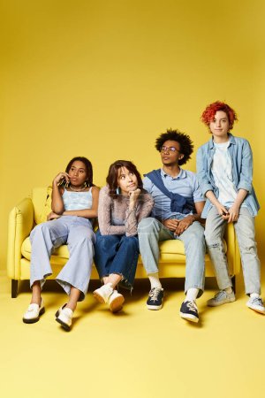 Photo for A group of young multicultural friends sit and laugh on top of a bright yellow couch in a stylish studio setting. - Royalty Free Image