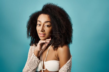 Attractive African American woman with curly hairdo posing on vibrant blue background.