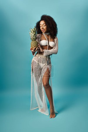 African American woman in white bikini holding pineapple.