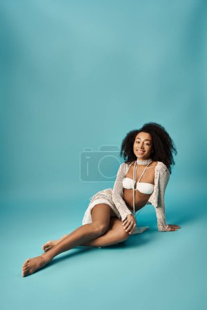 African American woman in trendy white bikini resting on a blue background.