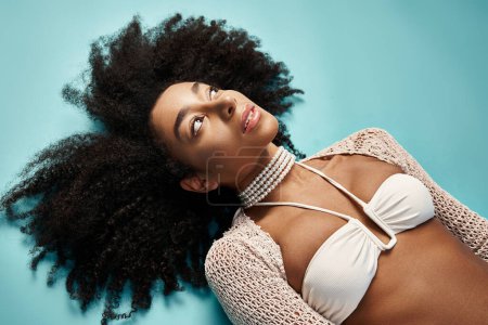 Foto de Mujer afroamericana en bikini de moda descansando sobre un vibrante telón de fondo azul. - Imagen libre de derechos