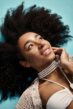Young African American woman with curly hairdo laying gracefully on a vibrant blue background.