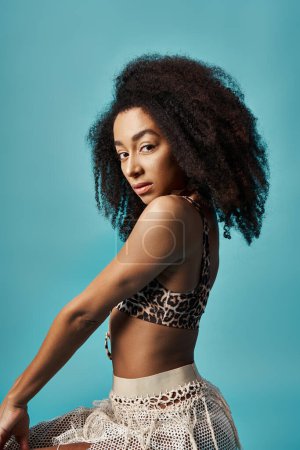 Téléchargez les photos : Jeune femme afro-américaine frappant une pose dans une jupe léopard sur un fond bleu vif. - en image libre de droit