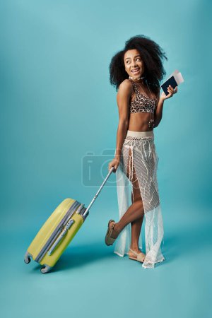 Young African American woman in a trendy swimsuit holding a suitcase.