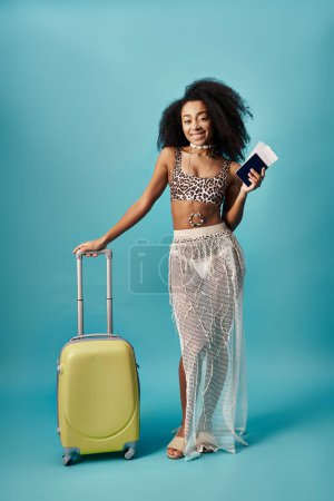Young woman with suitcase and passport posing on blue background