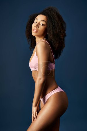 Joven mujer afroamericana posando en bikini rosa sobre un vibrante fondo azul.