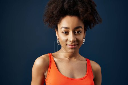 Téléchargez les photos : Jeune femme afro-américaine élégante en débardeur orange posant en toute confiance. - en image libre de droit