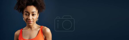 Téléchargez les photos : Une jeune femme avec une coiffure bouclée souriant sur un fond bleu vibrant. - en image libre de droit