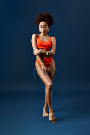 Stylish woman strikes a pose in orange swimsuit against blue backdrop.