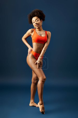 Photo for Stylish African American woman in orange bikini posing on vivid blue background. - Royalty Free Image