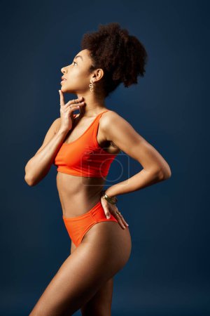 Téléchargez les photos : Femme afro-américaine élégante en bikini orange frappant une pose sur fond bleu. - en image libre de droit
