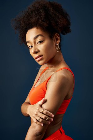 Téléchargez les photos : Élégante jeune femme afro-américaine pose avec confiance dans le haut orange coloré. - en image libre de droit