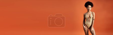 Téléchargez les photos : Femme afro-américaine élégante en maillot de bain à la mode pose sur fond orange vif. - en image libre de droit