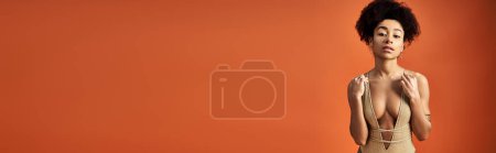 Photo for Stylish African American woman striking a pose in front of bright orange backdrop. - Royalty Free Image