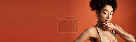 Foto de Joven mujer afroamericana posando en traje de baño de moda contra el vibrante fondo naranja. - Imagen libre de derechos