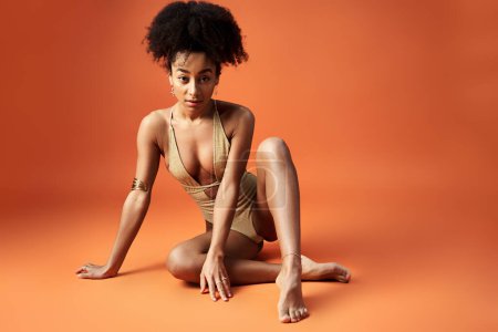 Téléchargez les photos : Femme afro-américaine élégante en bikini frappant une pose sur fond orange vif. - en image libre de droit