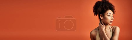 Photo for A stylish young African American woman with curly hairdo striking a pose against a vibrant orange backdrop. - Royalty Free Image