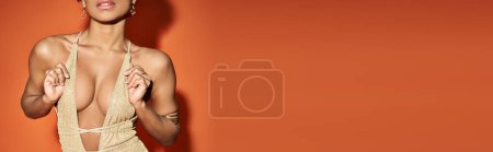Téléchargez les photos : Femme afro-américaine élégante en maillot de bain en or posant sur fond orange vif. - en image libre de droit