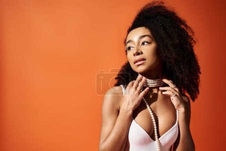 Stylish African American woman with curly hairdo striking a pose against an orange background.