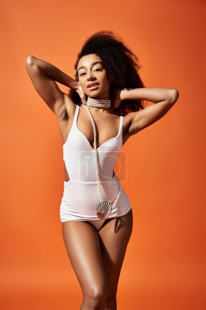 Téléchargez les photos : Femme afro-américaine en maillot de bain blanc frappant une pose sur fond orange vif. - en image libre de droit