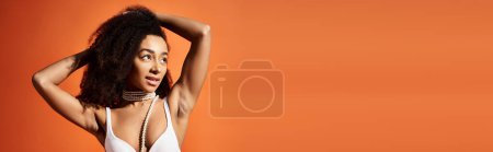 Vorstellung einer attraktiven Afroamerikanerin in einem trendigen weißen Bikini, die vor einem leuchtend orangen Hintergrund posiert.