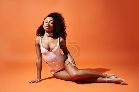 Stylish African American woman in white swimsuit striking a pose against vibrant orange background.