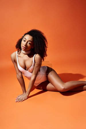 Téléchargez les photos : Femme afro-américaine élégante pose en maillot de bain blanc sur fond orange vif. - en image libre de droit