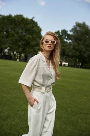 A graceful woman exudes elegance in a white jumpsuit and stylish sunglasses, embodying chic and sophistication.
