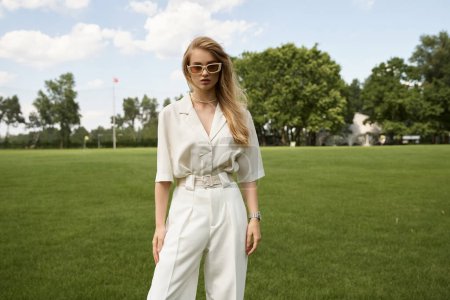 Photo for A stylish woman in a white jumpsuit stands gracefully in a lush grassy field during a serene outdoor outing. - Royalty Free Image