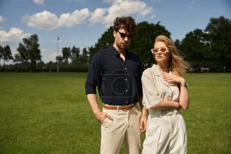 Téléchargez les photos : Un jeune couple élégant en tenue haut de gamme profiter d'un moment ensemble dans un champ vert luxuriant, incarnant un vieux style de vie de l'argent. - en image libre de droit