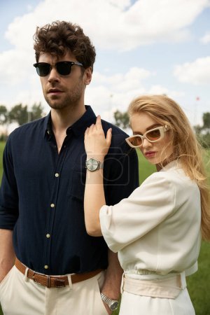 Ein stilvoller, wohlhabender Mann und eine Frau mit Sonnenbrille in einem üppigen Feld, die einen Hauch von Raffinesse und Luxus verströmen.