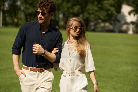 A stylish, well-dressed man and woman leisurely walk in a lush park, embodying a classic, affluent lifestyle.