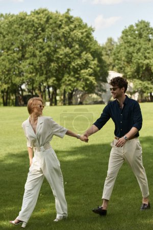 A stylish couple holds hands in a lush park, surrounded by greenery, embodying elegance and tranquility.