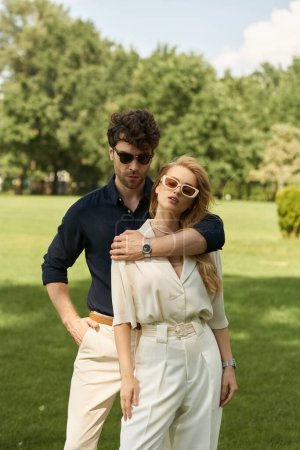 Elegante pareja vestida con un atuendo elegante posando al aire libre en un parque sobre una exuberante hierba verde. Abrazar el estilo de vida de los ricos.